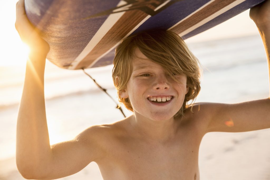 Boy carrying surfboard over head smiling